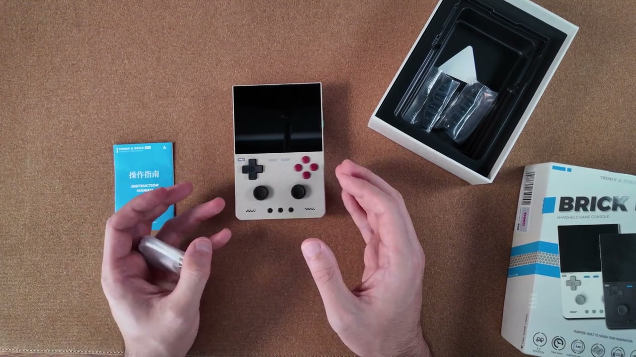 TrimUI Brick Pro von vorne in der Hand, Verpackung im Hintergrund